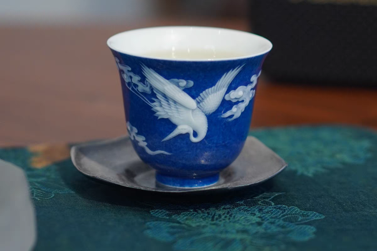 A blue and white ceramic cup with a bird pattern, placed on a saucer, on a floral patterned surface.