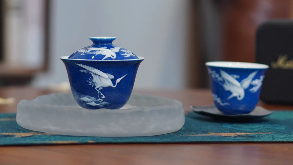 A blue and white ceramic cup with a bird pattern, placed on a saucer, on a floral patterned surface.